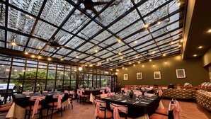 Un restaurant doté d’un plafond en verre, de tables décorées avec des serviettes roses et offrant une vue sur la verdure environnante.