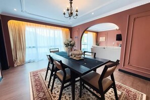 Un coin repas avec une table en bois foncé, des chaises rembourrées, un lustre et une grande fenêtre agrémentée de rideaux.