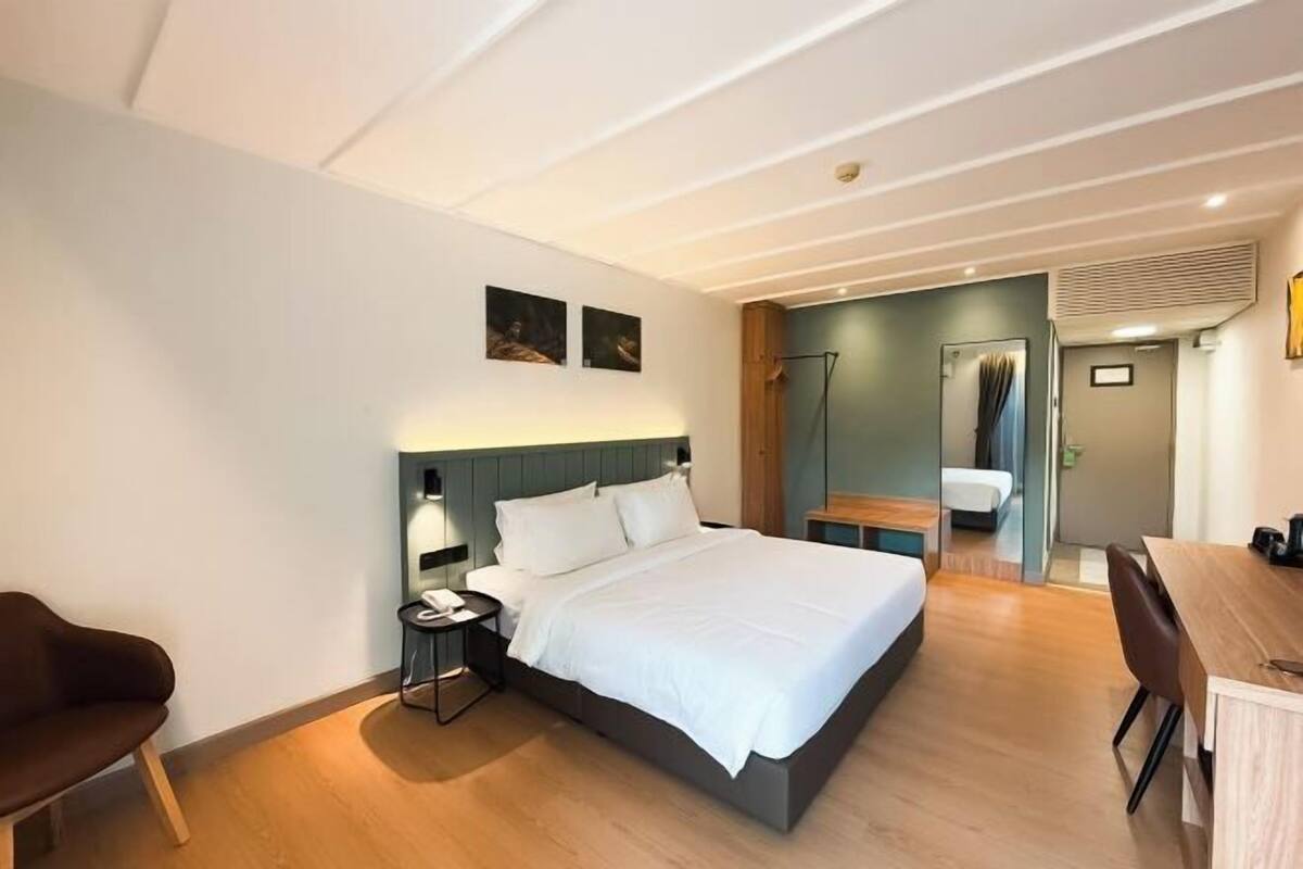 Een moderne hotelkamer met een bed, een bureau, een stoel, een nachtkastje en een wandlamp.