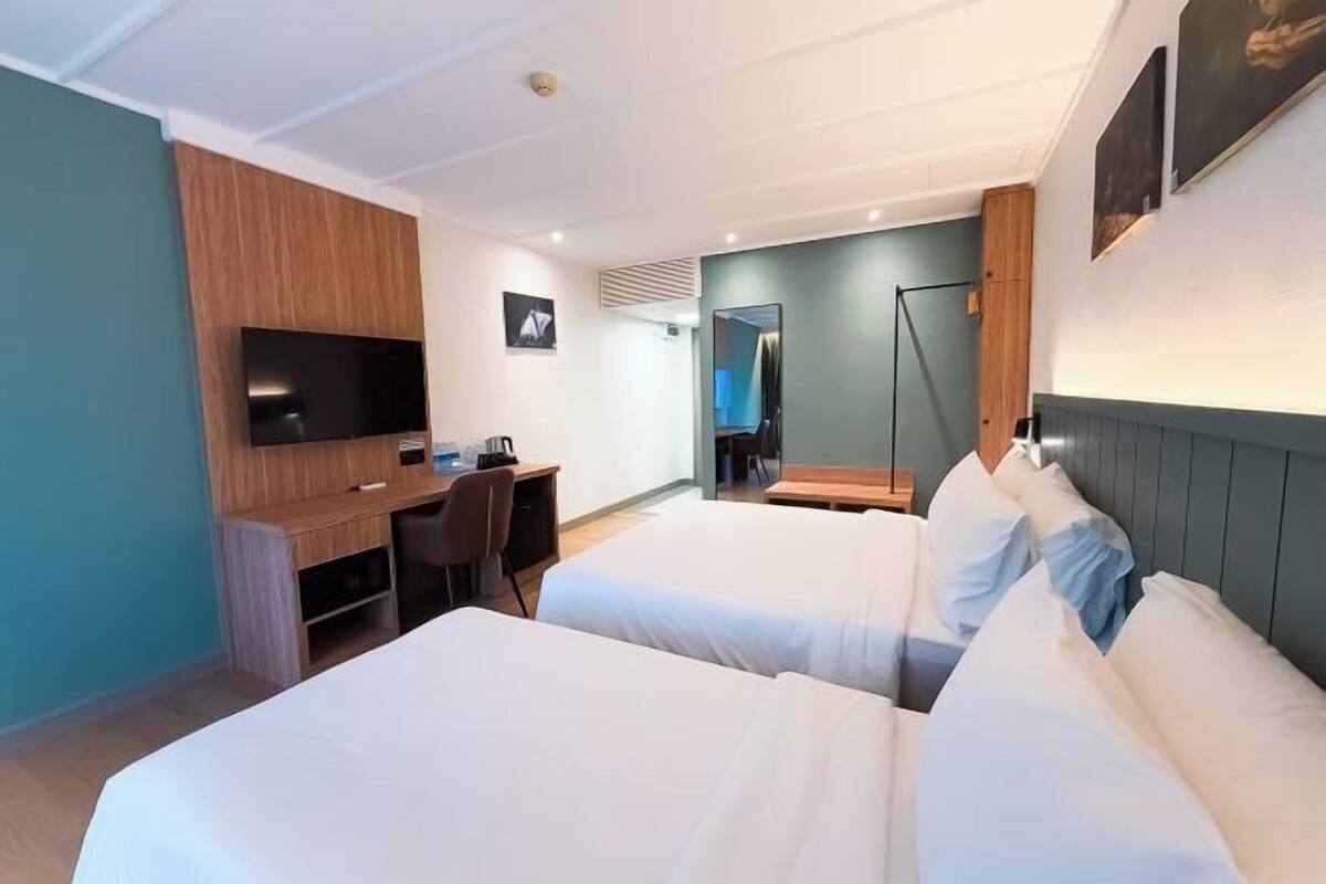 Een hotelkamer met twee bedden, een bureau, een televisie, een spiegel en een raam.