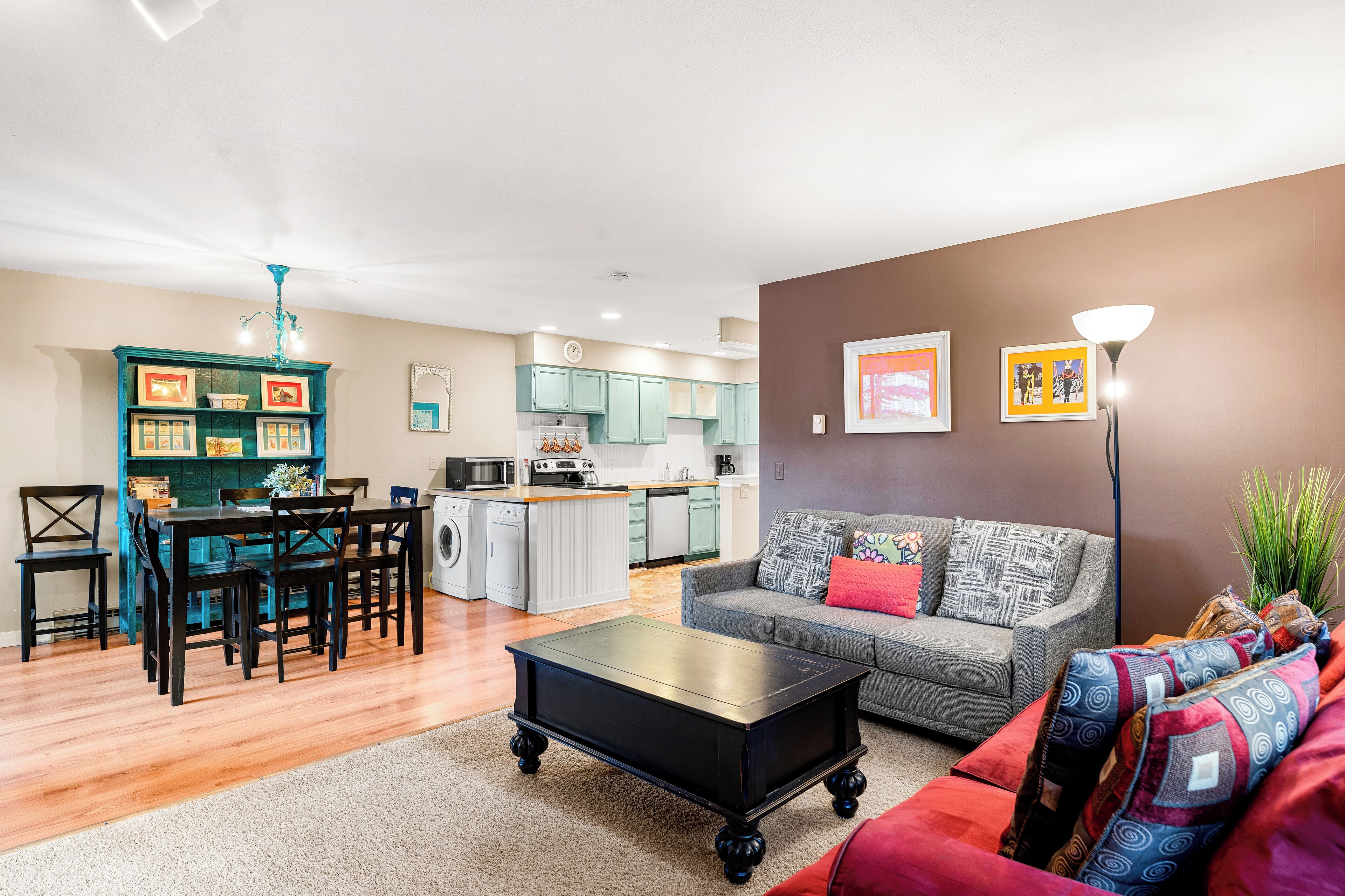 A modern living room with a grey sofa, a black coffee table, and a dining area with teal chairs and a table.