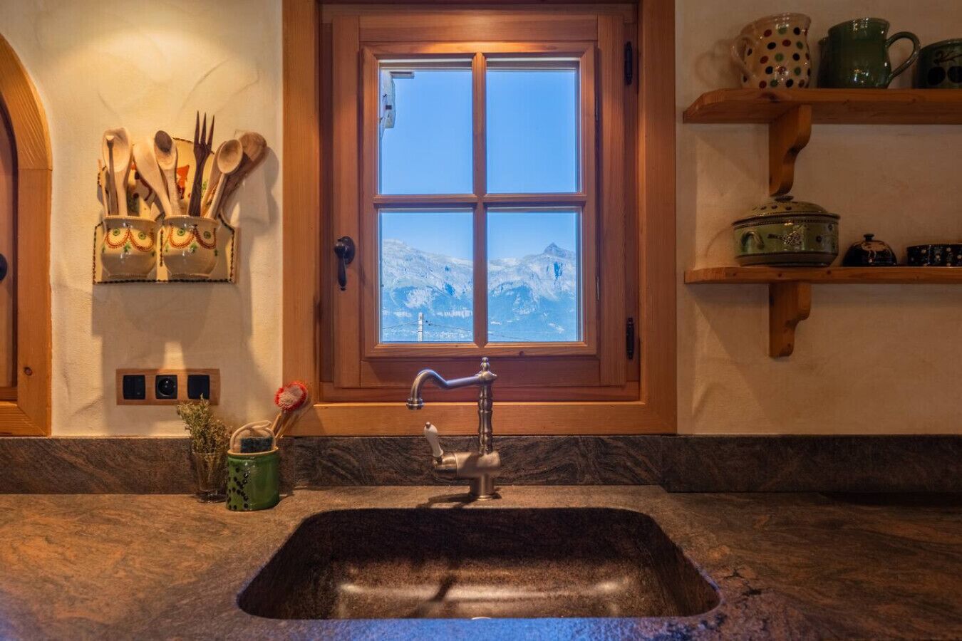 A kitchen with a granite countertop, a sink, and a window with a view of a snowy mountain.