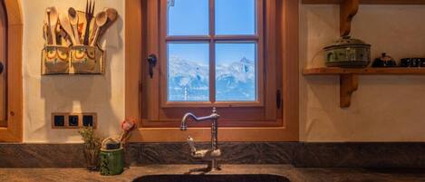 A kitchen with a granite countertop, a sink, and a window with a view of a snowy mountain.