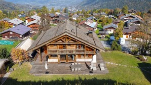 Een houten chalet met een balkon, omgeven door een weelderig groen gazon en een bergachtig landschap.