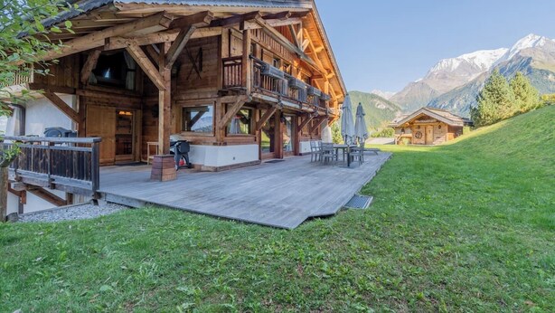 Een houten chalet met een balkon, een barbecueplaats en uitzicht op bergen.