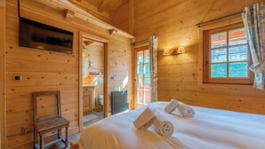 Een houten kamer met een bed, een stoel, een televisie en een raam met gordijnen.