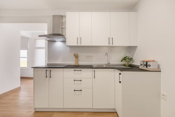 A modern kitchen with white cabinets, a black countertop, and a stainless steel range hood.