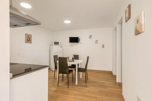 A compact kitchen with a microwave, a dining table with chairs, and a flat-screen TV mounted on the wall.