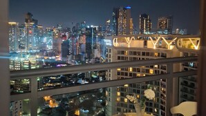 A high-rise hotel room with a city skyline view, a balcony with a table and chairs, and a large window. - Condo near Makati with Free pool & Rockwell View (Mandaluyong City)