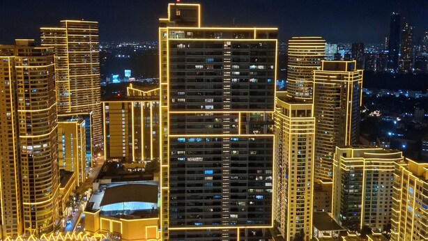 A high-rise building complex with multiple floors, illuminated by yellow lights, and surrounded by other buildings. - Condo near Makati with Free pool & Rockwell View (Mandaluyong City)