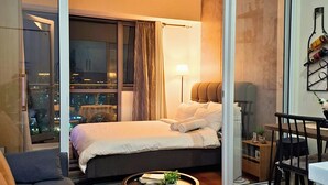 A modern hotel room with a bed, a sofa, a dining area, and a view of the cityscape. - Condo near Makati with Free pool & Rockwell View (Mandaluyong City)