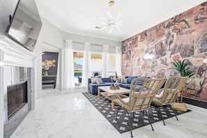 A modern living room with a fireplace, a blue sofa, wicker chairs, and a mural wall.