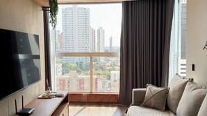 Ett modernt hotellrum med en stor TV, ett skrivbord i trä, en soffa och utsikt över stadsbilden.