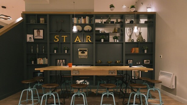 A bar area with a wooden counter, stools, and shelves filled with books and decorative items. - Student Only College Green (Bristol)