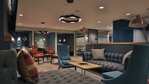 A modern living room with a sofa, armchairs, and a coffee table. There are pendant lights and a television mounted on the wall. - Student Only College Green (Bristol)