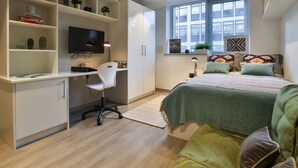 A modern bedroom with a desk, chair, bed, and shelving with plants. - Student Only College Green (Bristol)