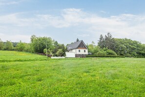Una casa con techo inclinado, rodeada por un campo cubierto de césped y árboles.