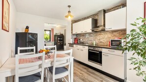 Une cuisine moderne avec des meubles blancs, un pare-feu en pierre et un coin repas agrémenté d’une nappe à carreaux.