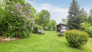 Une petite cabane dotée d’une terrasse en bois, entourée d’une végétation luxuriante et d’arbustes en fleurs.