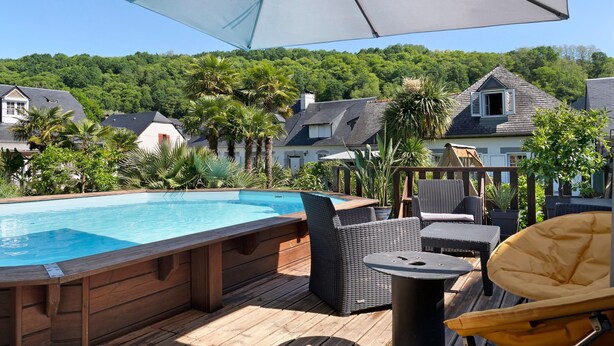 Une terrasse en bois avec une piscine, des meubles en osier et un grand parasol.
