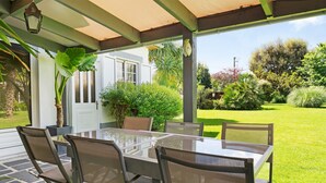 Une terrasse extérieure avec une table et des chaises en verre, entourée de verdure et offrant une vue sur un jardin.