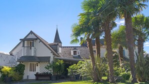 Une maison à deux étages, dotée d’un toit à forte pente, d’une cheminée bien visible et d’un petit balcon.