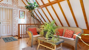 Une pièce chaleureuse avec un plafond haut, des poutres en bois, des meubles en osier et une plante en pot.