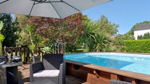 A wooden deck with a pool, wicker furniture, and a pergola with a white umbrella.