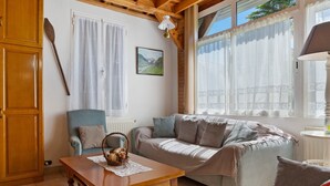 A cozy living room with a wooden table, a sofa, a chair, and a window with curtains.
