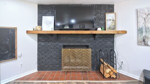 Een woonkamer met een zwart metselwerk schouw, een tv aan de muur en een houten plank erboven.