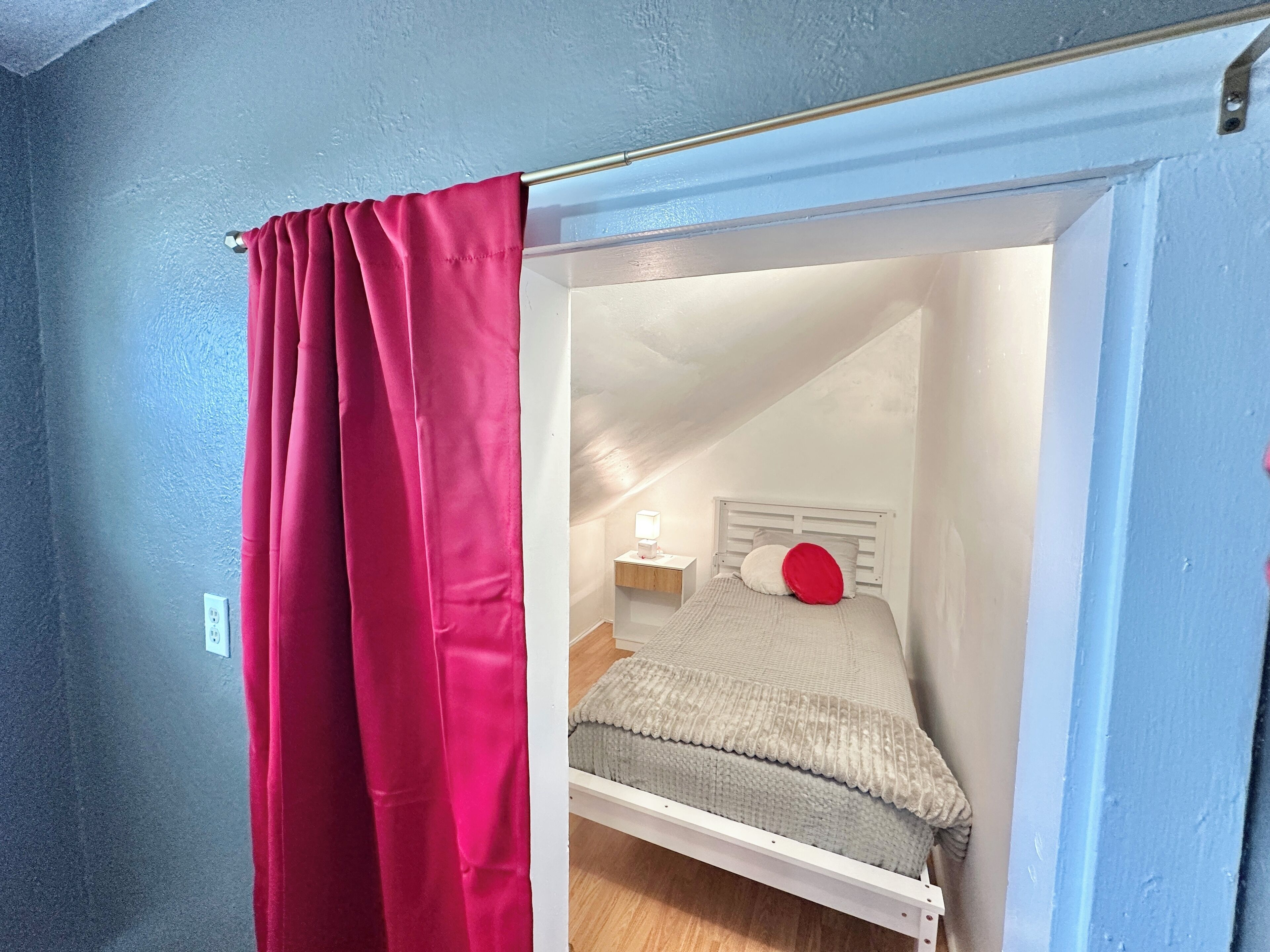 A bedroom with a bed, a nightstand, and a red curtain.