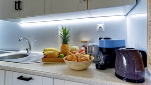 A kitchen with a sink, a coffee maker, a toaster, and a bowl of bread and fruit. - KATAL waterfront - T2 Comfort - Elegance (Sainte-Luce)