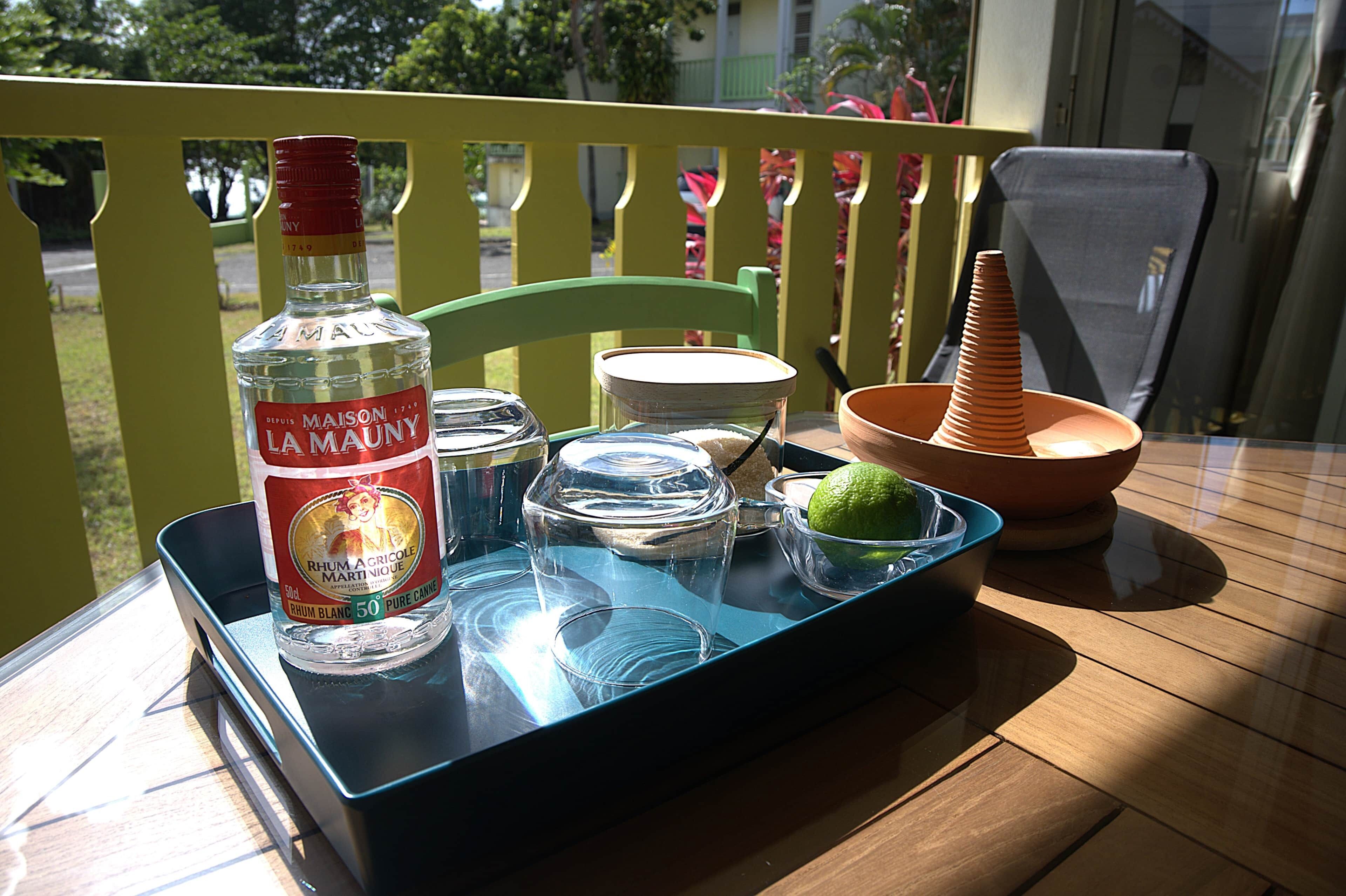 A table with a bottle of Maison La Mauny, a glass container, a bowl, and a lime on a tray.