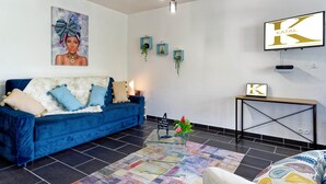 A modern living room with a blue sofa, a glass coffee table, and a TV mounted on the wall. - KATAL waterfront - T2 Comfort - Elegance (Sainte-Luce)