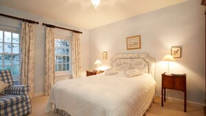 Une chambre avec un grand lit, deux tables de chevet avec des lampes, une chaise et une fenêtre avec des rideaux.