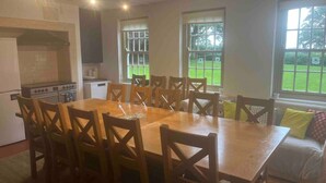 Une cuisine spacieuse avec une grande table à manger et des chaises, un four encastré et une vue sur une pelouse verdoyante grâce à de grandes fenêtres.