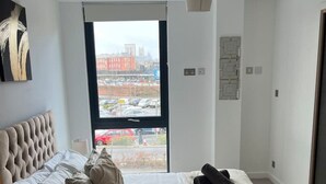 Een moderne slaapkamer met een groot bed en uitzicht op de stad door een raam, met een stadsgezicht zichtbaar buiten.