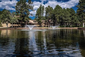 A tranquil outdoor setting with a pond, fountains, and a building with a wooden deck. - Innsbrook Vacation Townhome 104 (Ruidoso)