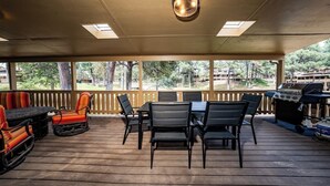 Un espace extérieur abrité, équipé d’une table et de chaises, d’un barbecue et offrant une vue sur le paysage environnant.