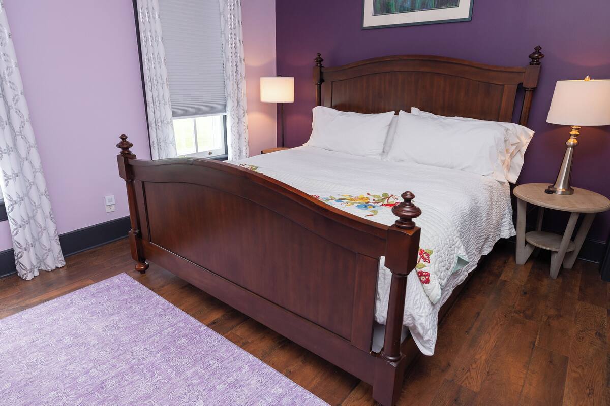 A neatly made bed with a wooden headboard, a bedside table with a lamp, and a window with curtains.