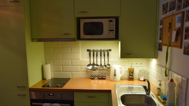 Una cocina con gabinetes verdes, un microondas, un fregadero y varios utensilios de cocina.
