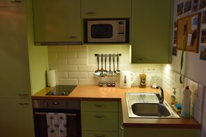 A kitchen with green cabinets, a microwave, a sink, and various kitchen utensils. - Beautifully Designed 1-bed Apartment by Vy Ehrad (Prague)