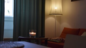 Una habitación de hotel con una cama, una mesa con una vela, una lámpara y vistas a un edificio a través de una ventana con cortinas.