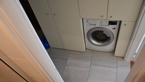 Un lavadero pequeño con lavadora de carga frontal, armarios color beige y suelo de baldosas.