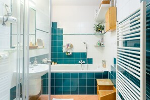 A modern bathroom with a glass shower enclosure, a white sink, a bathtub, and a wooden shelf with toiletries. - Premium Apartment With Private Terrace in Zizkov (Prague)
