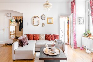 A modern living room with a sofa, a coffee table with decorative items, a chandelier, and a mirror on the wall. - Premium Apartment With Private Terrace in Zizkov (Prague)