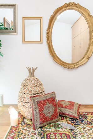 Ein Zimmer mit einem großen, verzierten Spiegel, einem gewebten Dekorationsobjekt und gemusterten Kissen auf einem farbenfrohen Teppich.