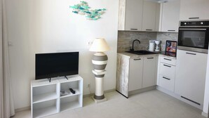 Une cuisine moderne avec des armoires blanches, un four encastré et un téléviseur à écran plat posé sur un meuble blanc.