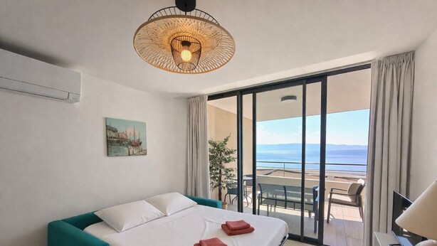 Une chambre d’hôtel avec un lit, une vue sur la mer, un tableau au mur et un luminaire au plafond.