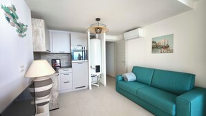 Un espace de vie compact comprenant un coin cuisine, un canapé de couleur turquoise et un tableau accroché au mur.